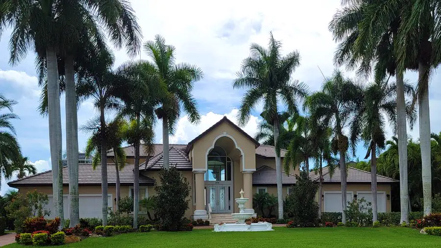 Large house set behind tall royal palm trees and a green lawn