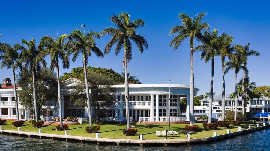 White waterfront house with columns, palm trees and a green lawn