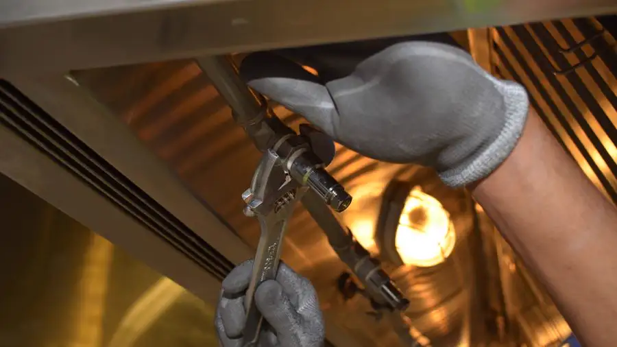 Gloved hand using a wrench on metal ducting