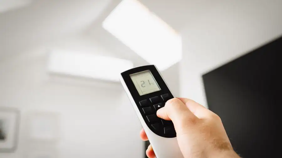 Hand holding a remote to set an air conditioner indoors