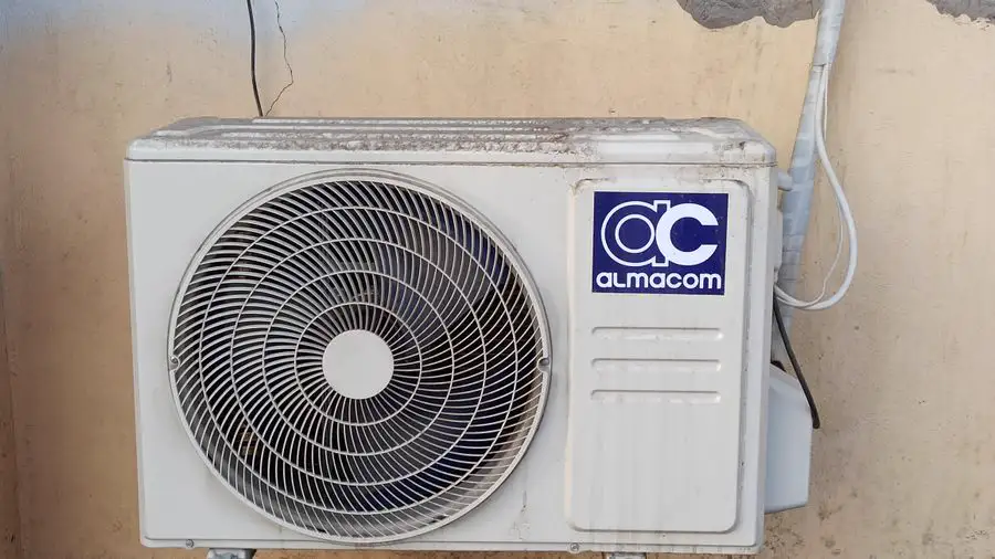 Well-worn outdoor air conditioner mounted on a wall with its lines running out the side
