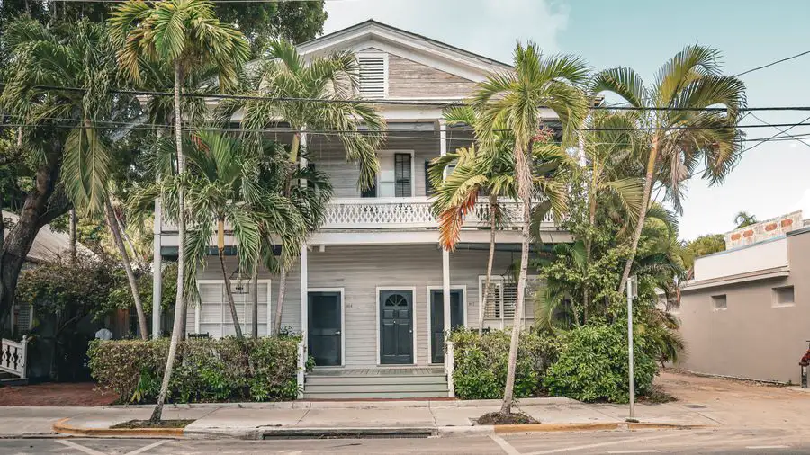 Two-story house with a porch, surrounded by palm trees on a street