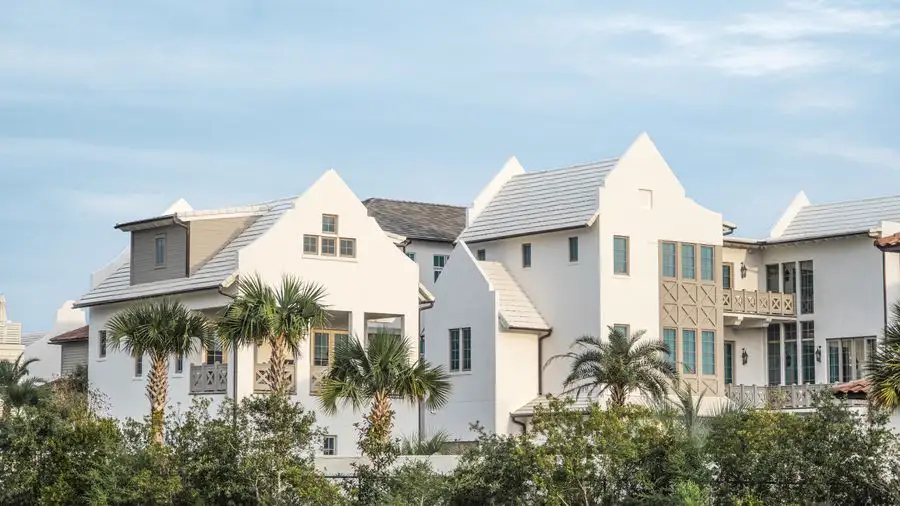 White multi-gabled house with a gray roof behind palms and shrubs