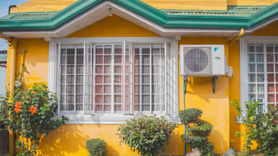 Yellow house with green trim and a wall-mounted air conditioner beside the window