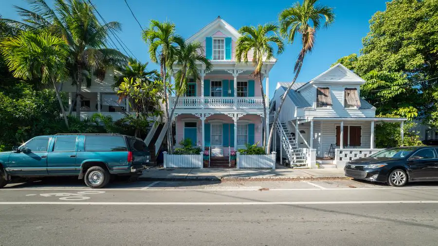 Blue and white three-story house with balconies and palm trees along a street