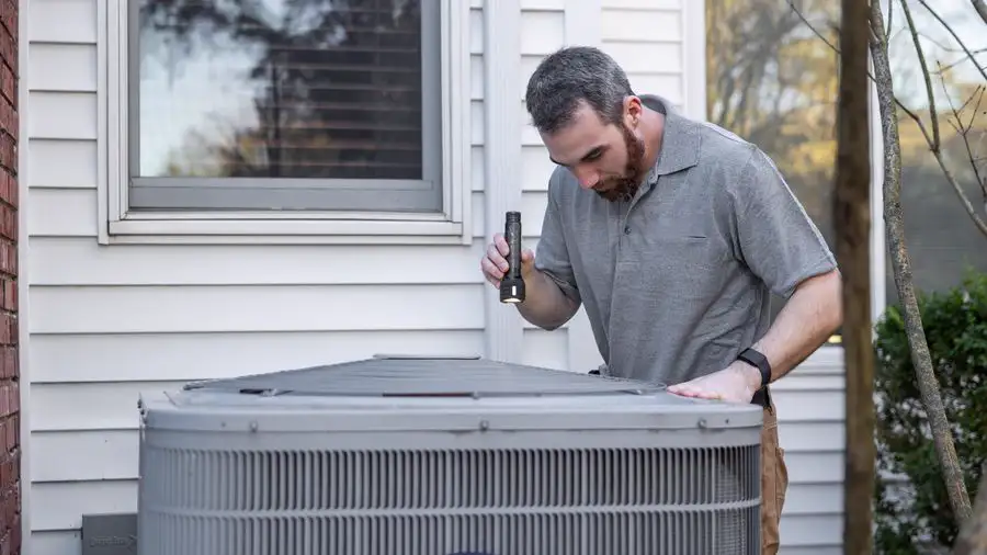 Technician inspecting the outdoor condenser unit beside a white house