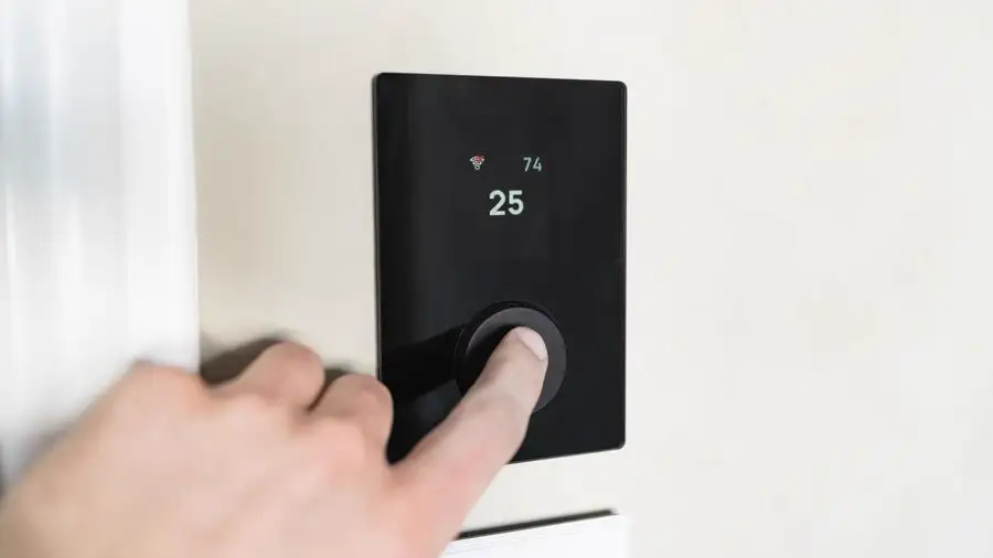 Hand pressing the button on a black digital control panel mounted on a white wall