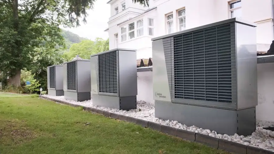 Row of gray outdoor heat pump units on the lawn beside a house