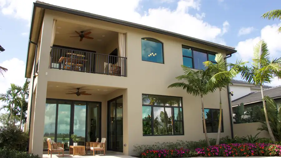 Two-story stucco house with a balcony, palm trees and flower beds
