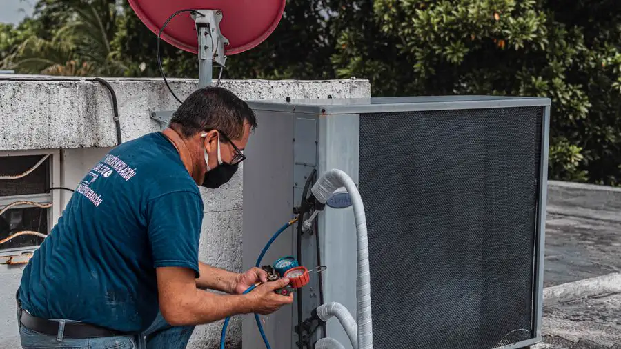 Technician in a face mask working on an outdoor air conditioner with a manifold gauge set