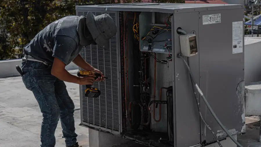 Worker in a bucket hat repairing an outdoor air conditioner on a rooftop