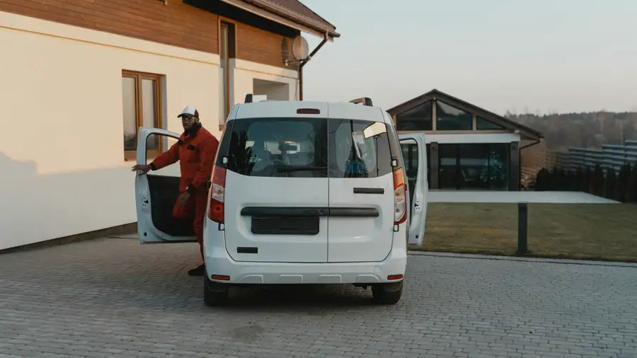 Worker in a red uniform stepping out of a white service van parked in a residential driveway