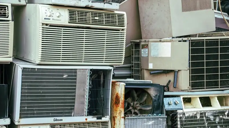 A collection of broken and rusted air conditioners piled in an outdoor junkyard
