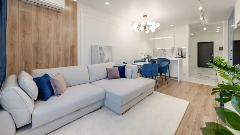 Contemporary living room with stylish furniture, elegant chandelier, and open kitchenette