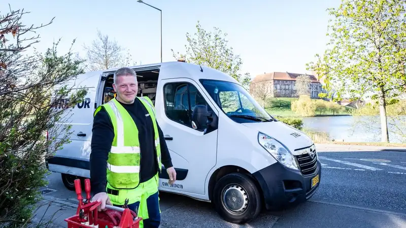 Smiling worker in reflective vest stands by a van holding tools