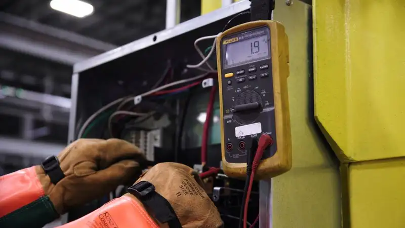 Electrician using a multimeter to fix industrial control panel wiring