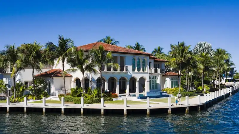 Elegant waterfront mansion in Fort Lauderdale, surrounded by palm trees and bright skies