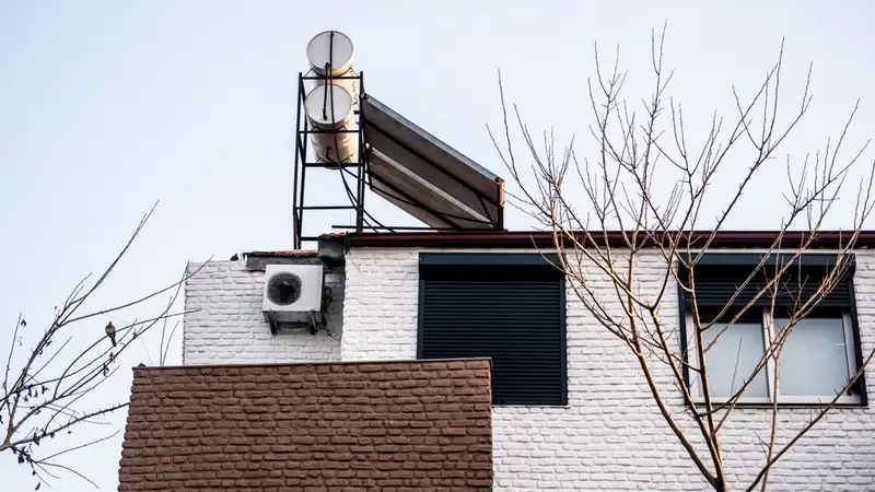 A minimalist building facade with air conditioner and bare winter trees, viewed from a low angle