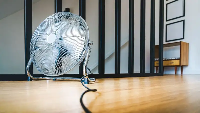 A sleek electric fan placed on a wooden floor in a modern indoor setting, providing comfort and cooling
