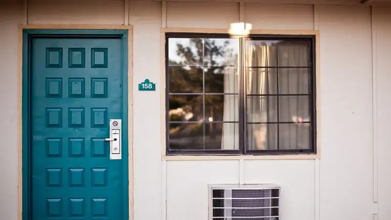 Teal door and window on a low building, with a window air conditioner below the window