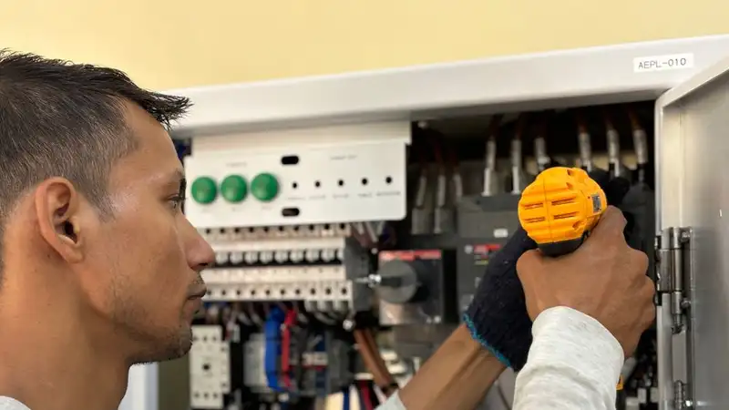 Skilled electrician using a drill to repair electrical equipment indoors. Focus on precision and safety