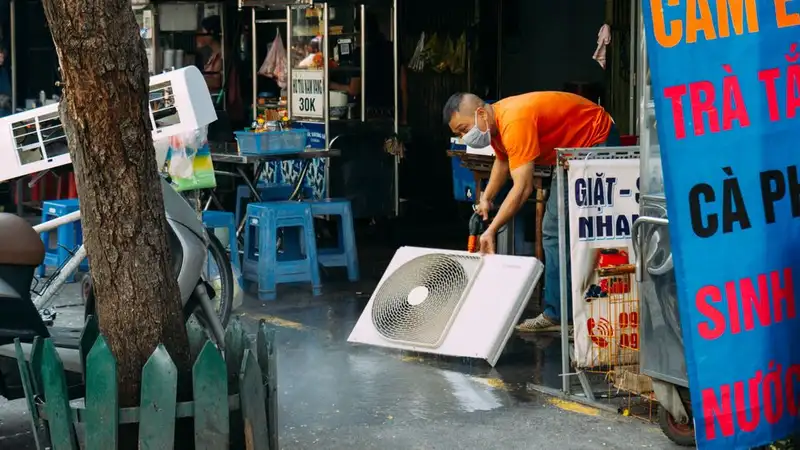 A man cleans a fan on a vibrant urban street with market stalls