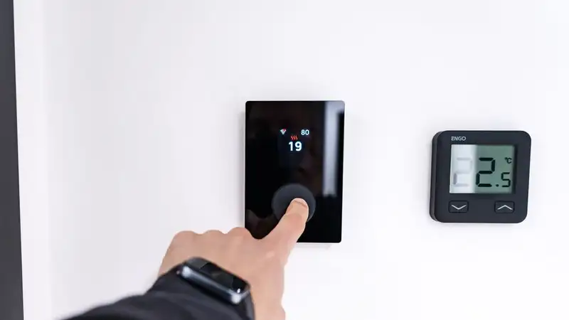 A hand adjusting a digital thermostat in a modern home interior, showcasing smart home technology