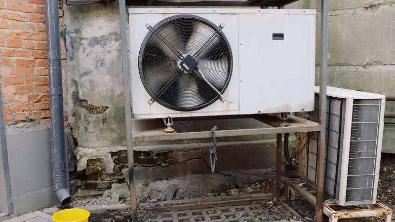 External air conditioner unit placed on metal platform near gray shabby wall of modern building on street
