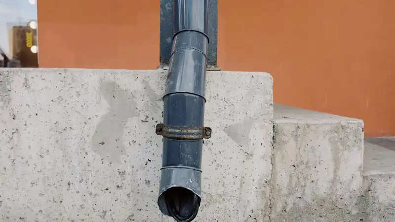 Aged metal drain pipe on a concrete wall with water stains, highlighting urban decay