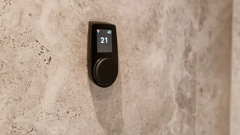 Close-up of a modern sauna temperature control device mounted on a textured stone wall, displaying a digital readout