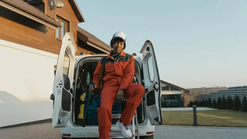 A professional worker in protective gear sits by a work van in a residential area