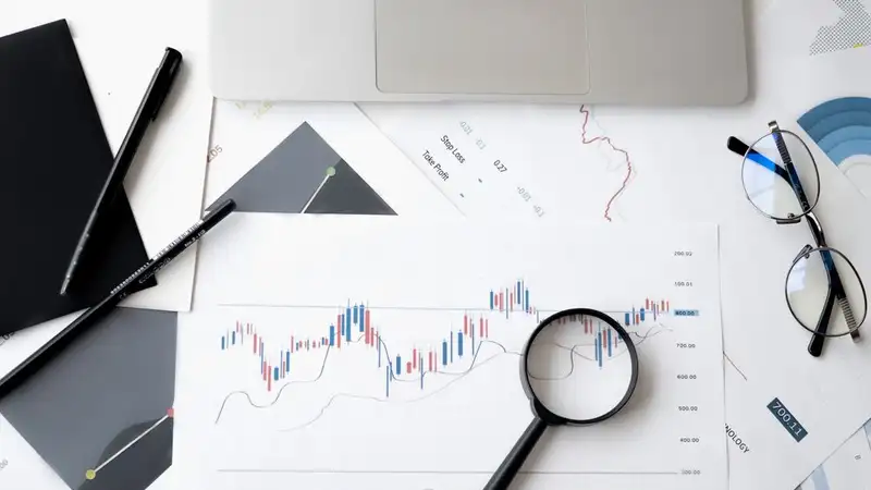 Flat lay of stock market analysis documents with magnifying glass, pens, and glasses