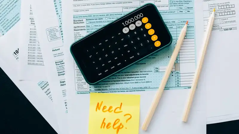 Top view of financial papers with a calculator, pencils, and a note saying 'Need help?' indicating tax or accounting assistance