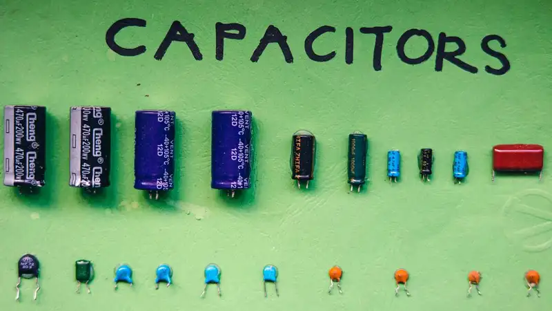 Rows of electronic capacitors of different sizes laid out on a green background