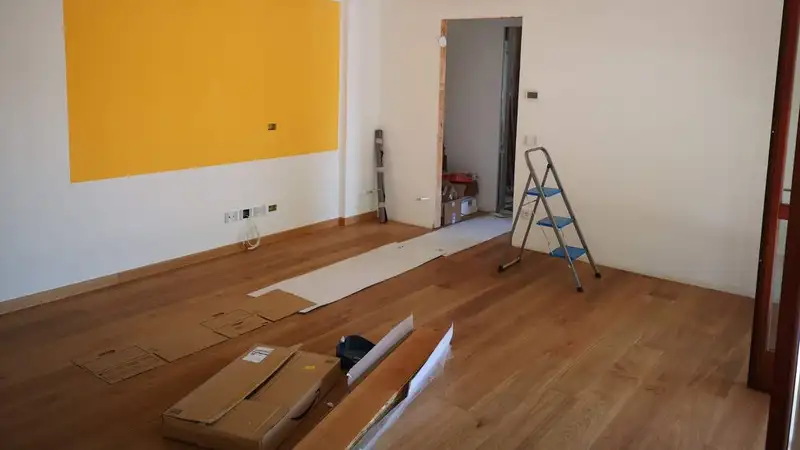 A bright, empty room under renovation with ladder, tools, and wooden flooring